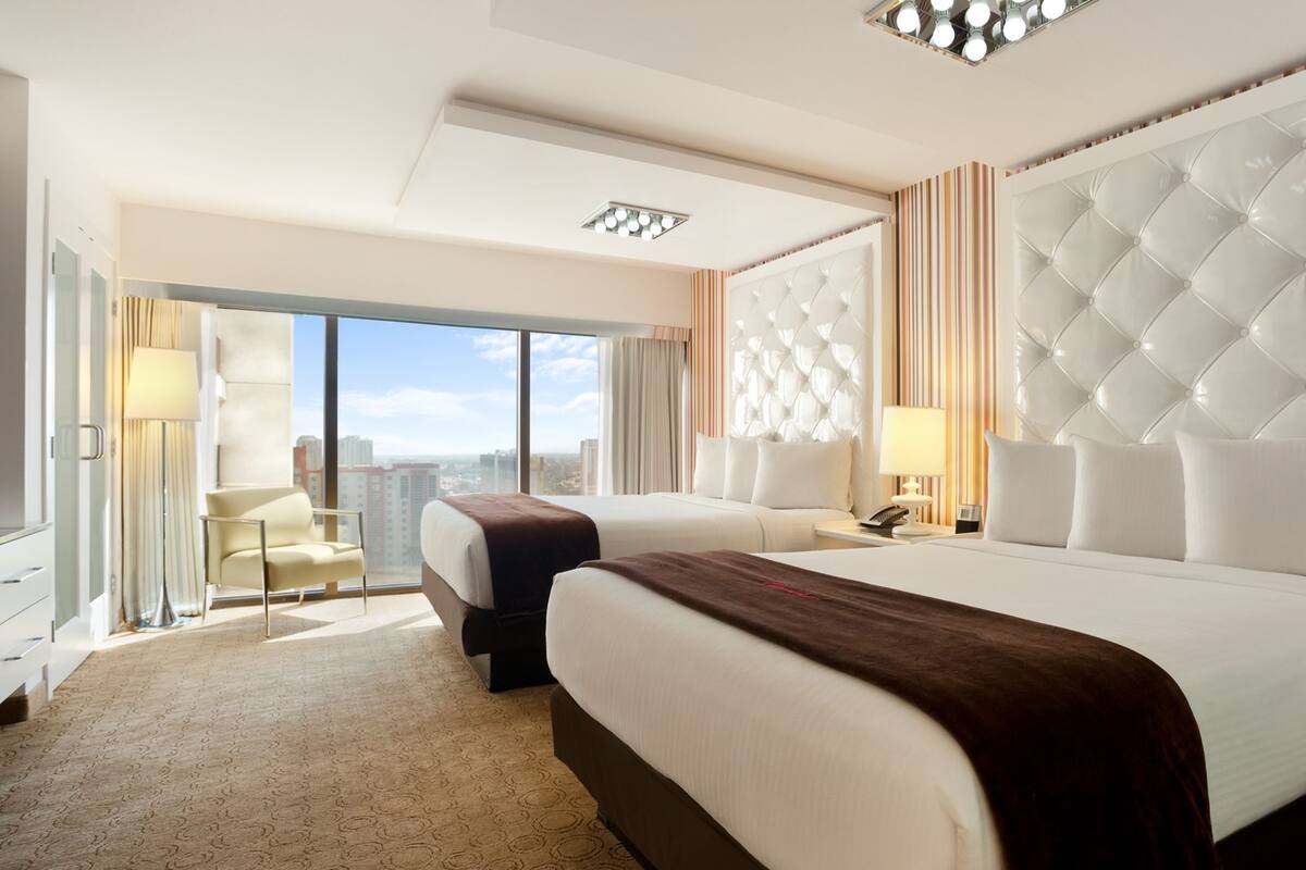 A hotel room with two beds, a large window with a city view, a modern chandelier, and a large mirror.