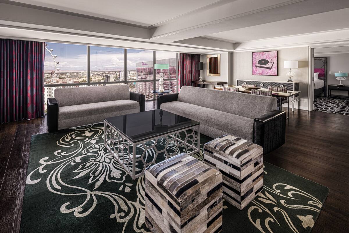 A spacious living room with a large window, a sofa, ottomans, a coffee table, and a view of the city.