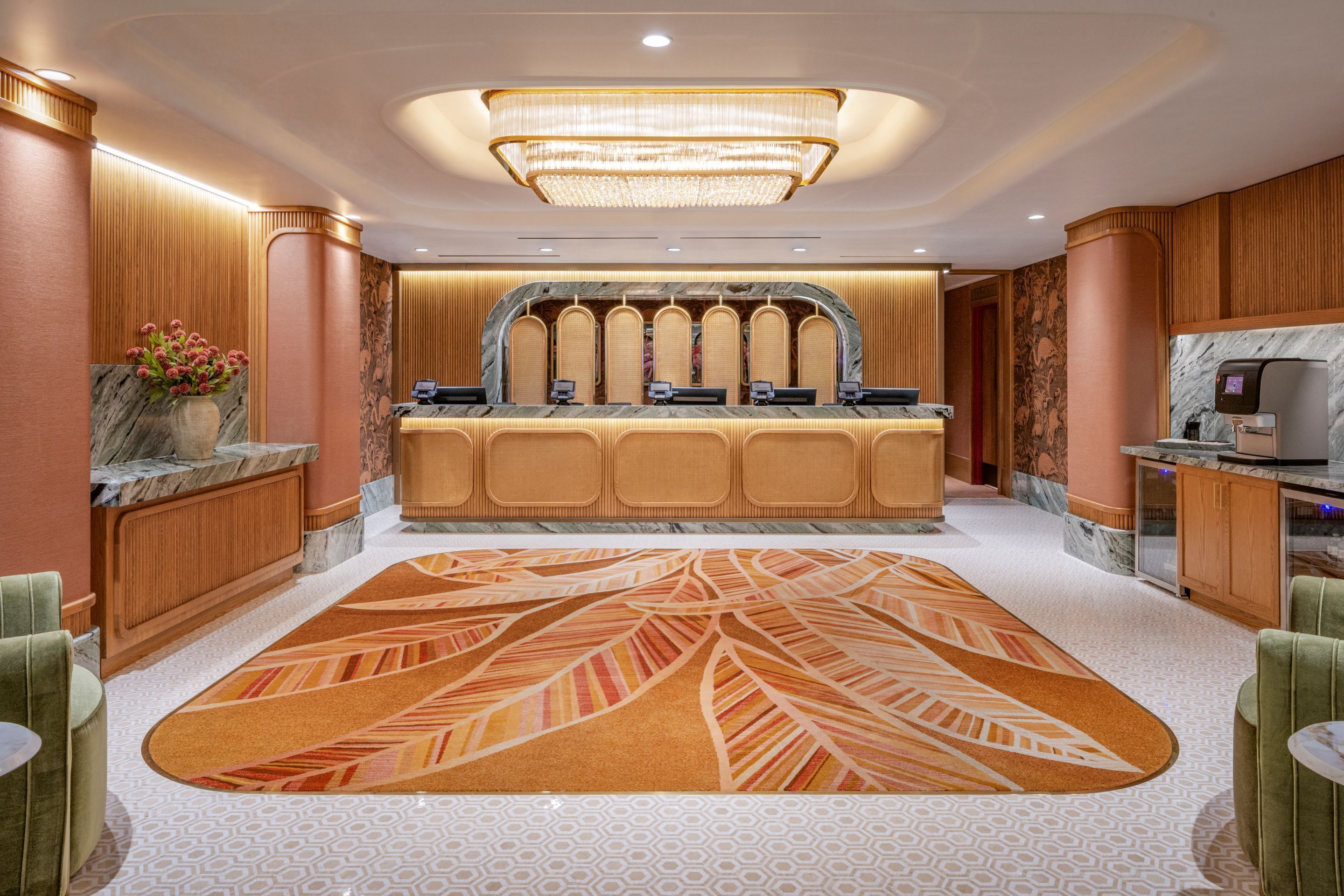 A hotel reception area with a marble counter, a large chandelier, and a patterned carpet.