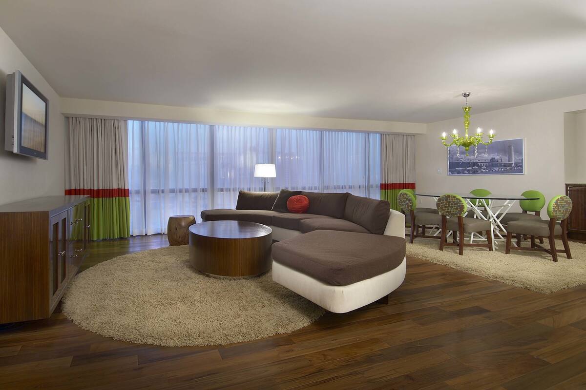 A modern living room with a sectional sofa, a round coffee table, a dining table with chairs, and a chandelier.