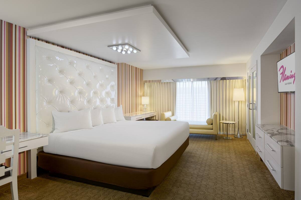 A hotel room with a large bed, a desk, a chair, a sofa, and a minibar.