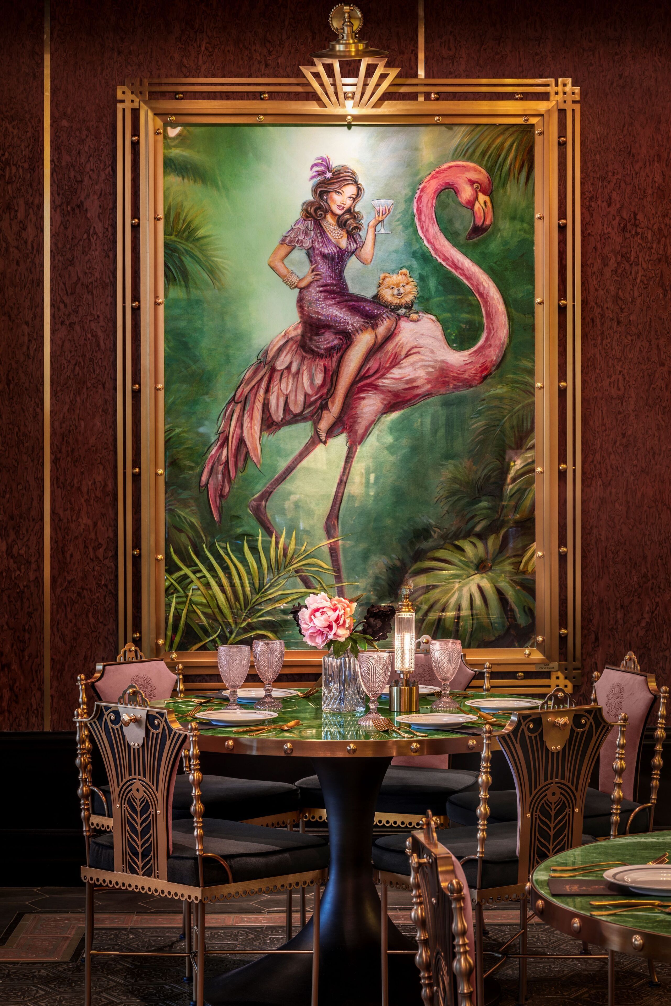 A dining area with a table set for four, surrounded by ornate chairs. A large painting of a woman with a flamingo is on the wall behind the table.