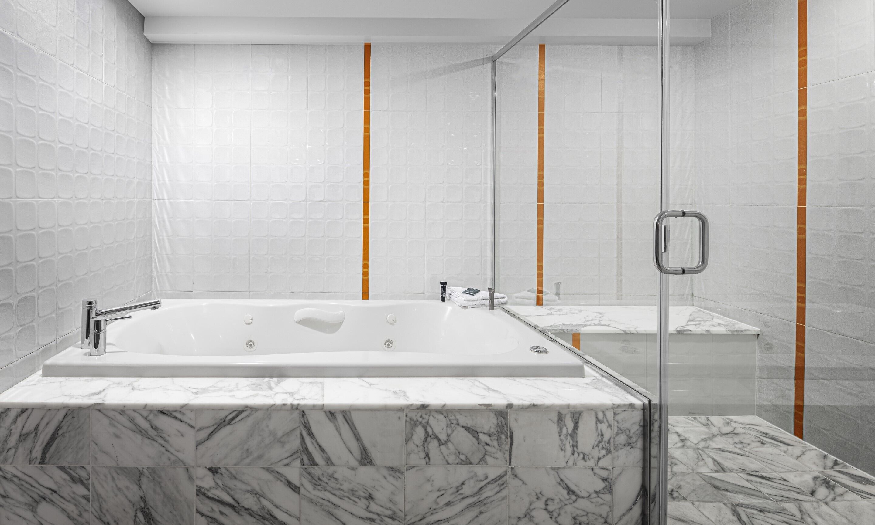 A modern bathroom with a marble bathtub, a glass shower enclosure, and a marble-tiled floor.