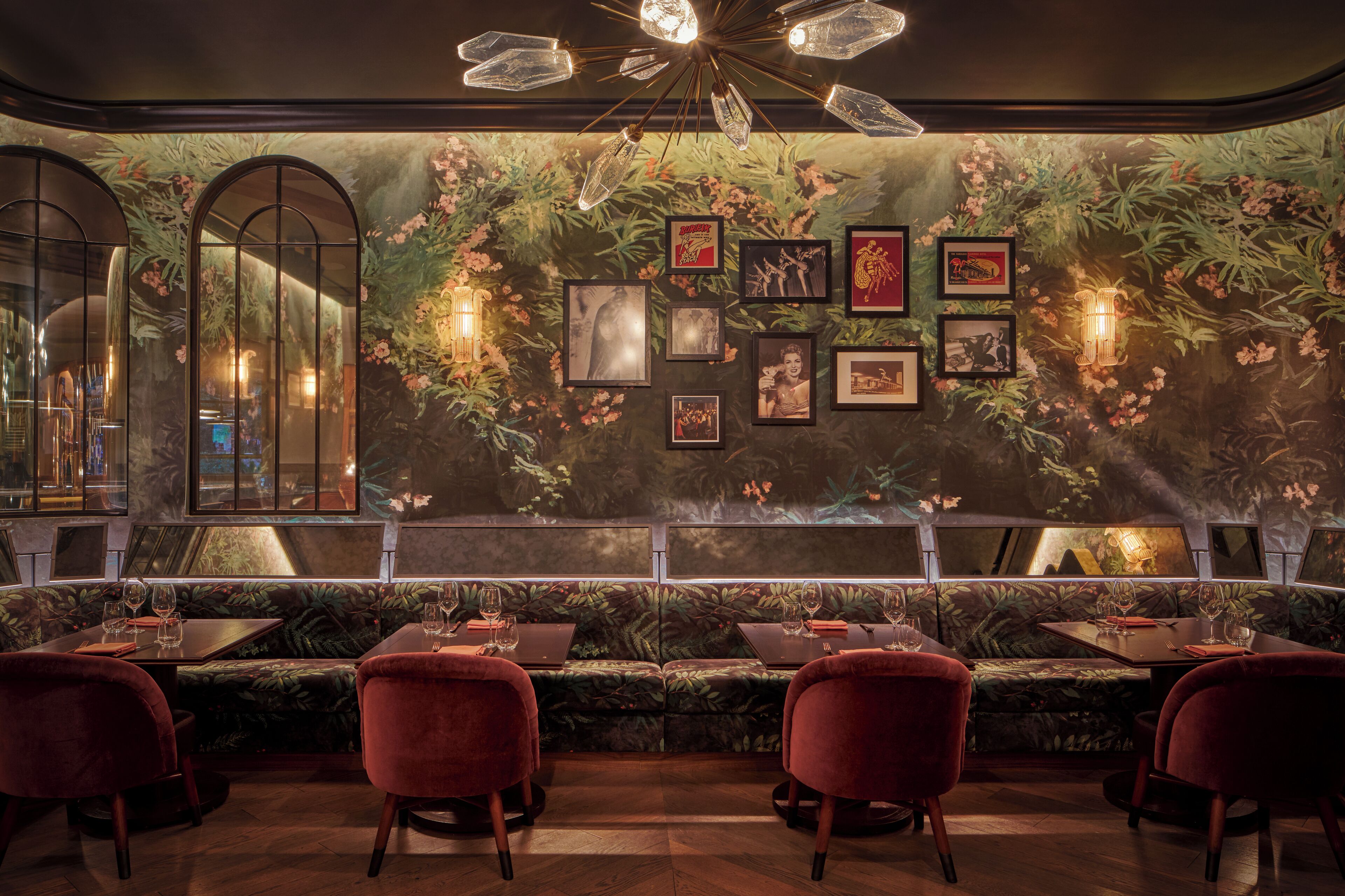 Un restaurante con un mural tropical, cuadros enmarcados y una zona de estar con mesas y sillas.