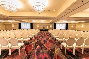 Une salle de conférence avec des rangées de chaises blanches, un sol recouvert de moquette et des lustres.