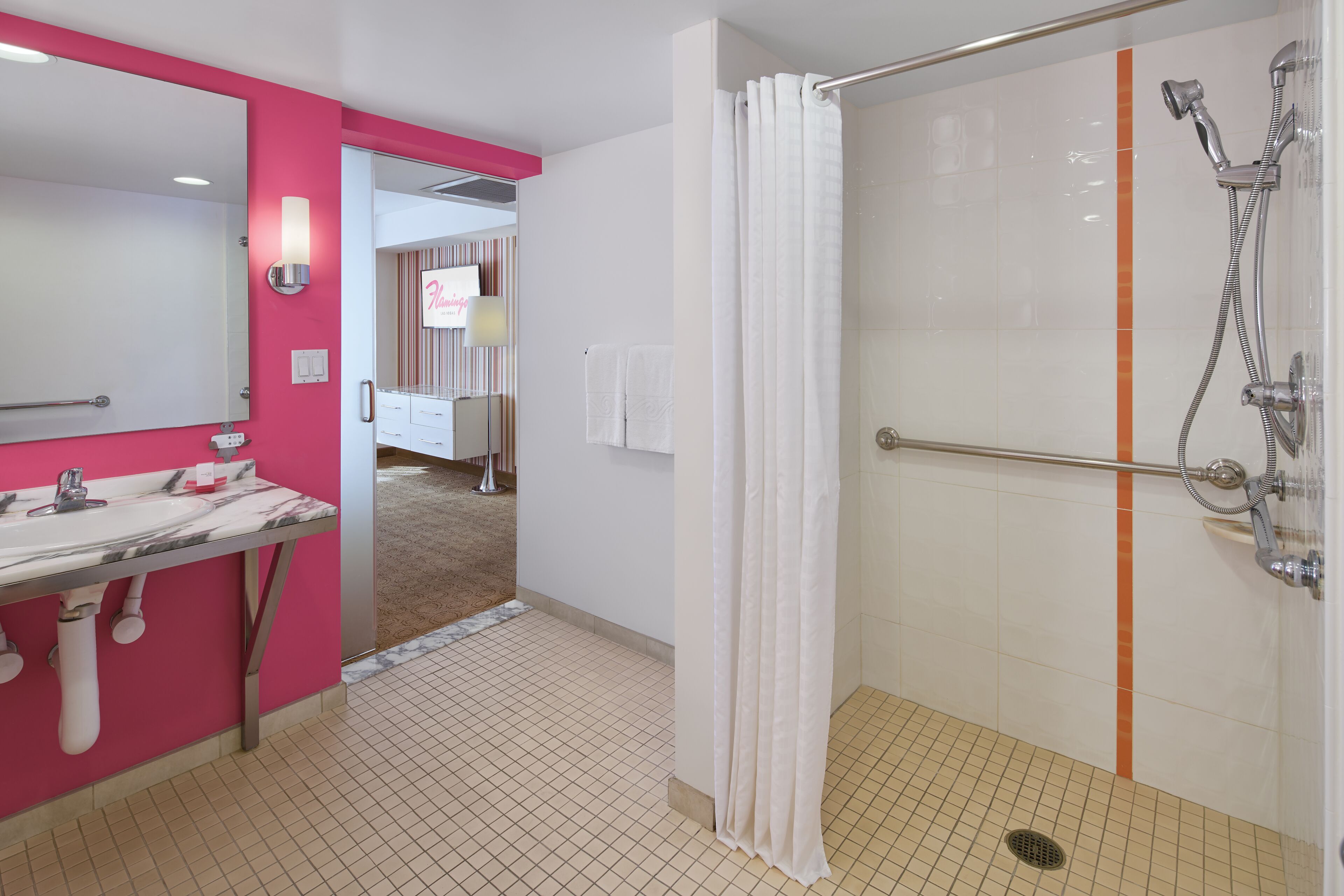 A modern bathroom with a pink vanity, a large mirror, a shower with a handheld showerhead, and a white curtain.