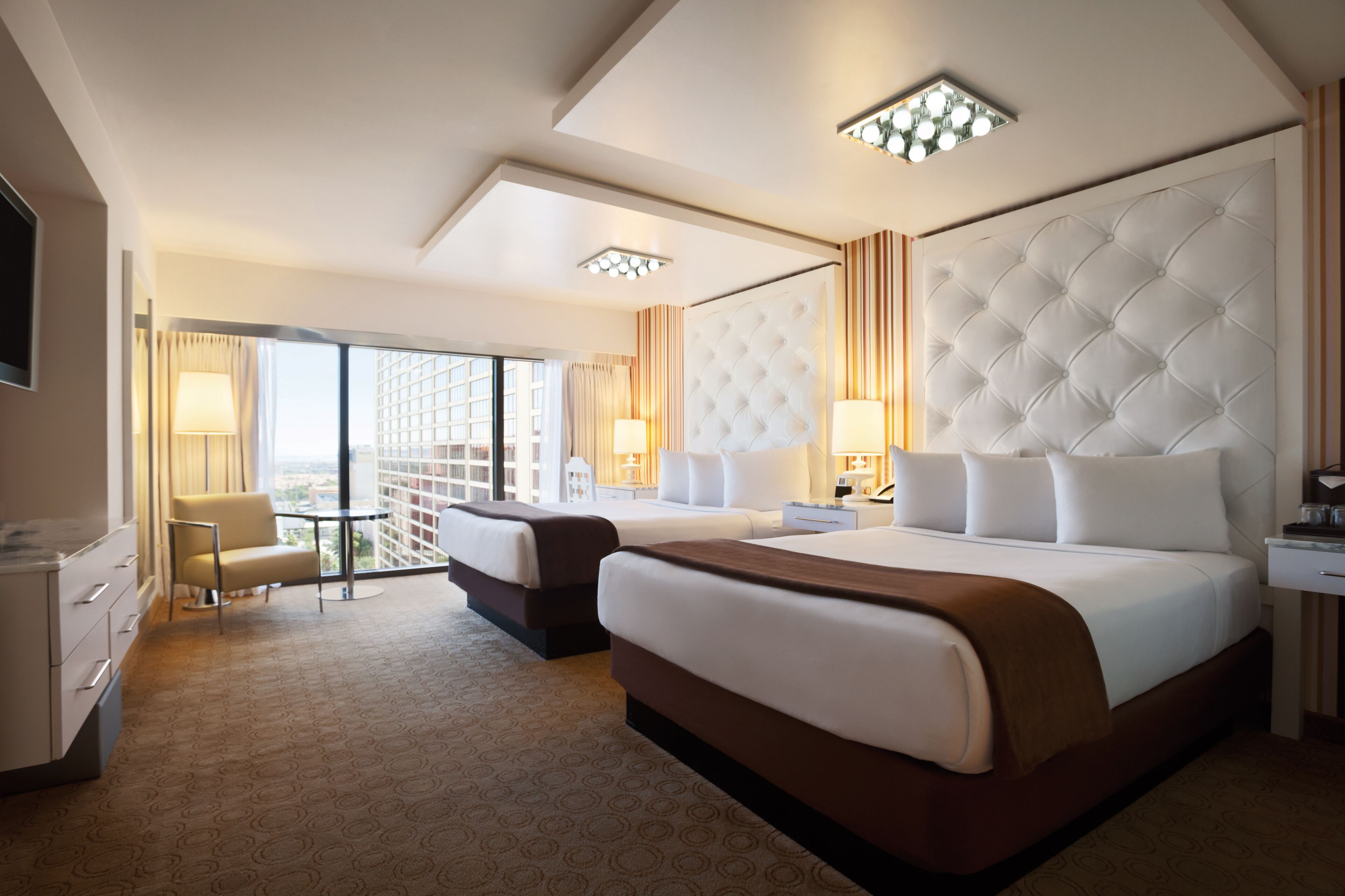 A hotel room with two beds, a desk, a chair, and a large window with a view.
