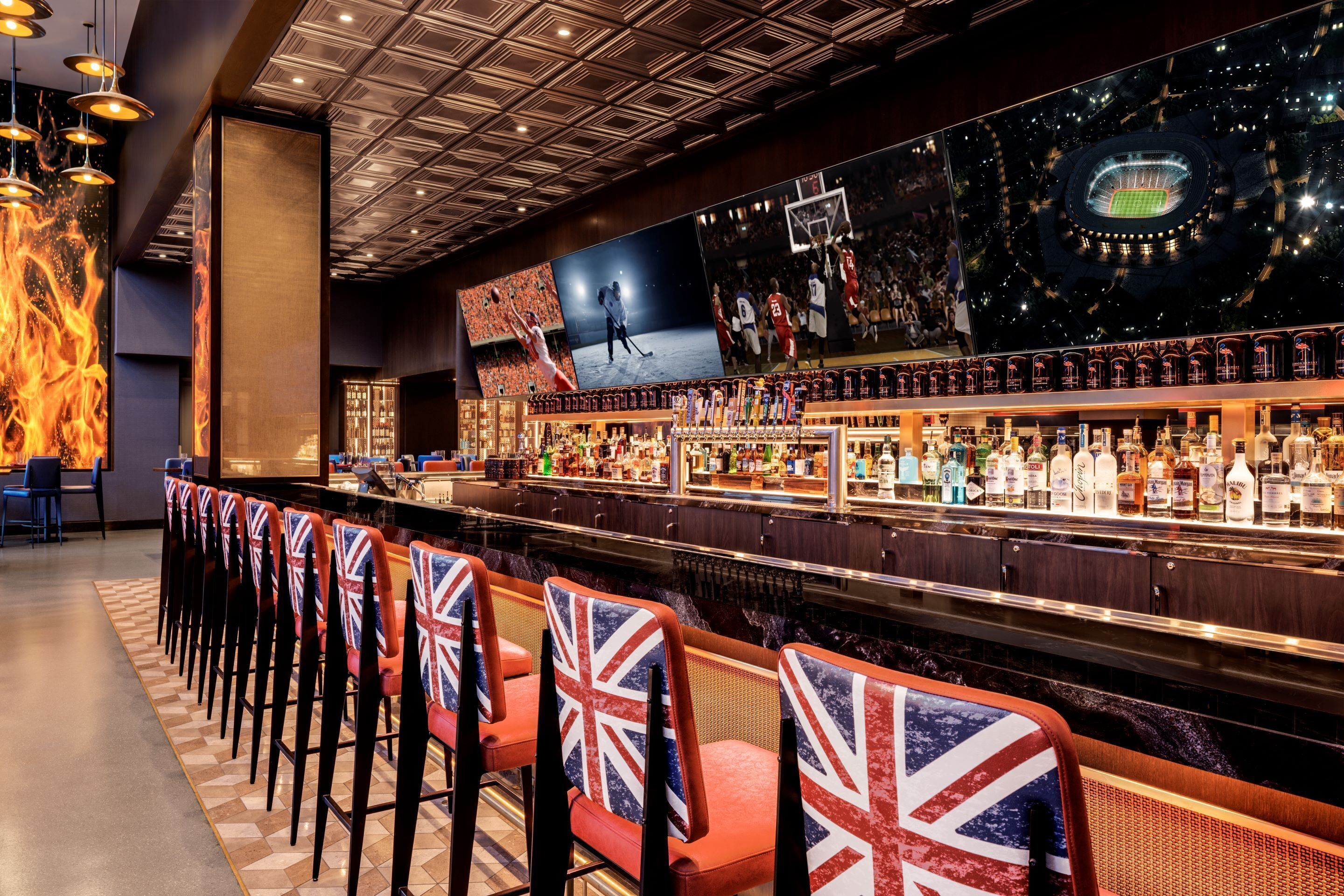 Un espace bar doté d’un long comptoir, de nombreuses bouteilles d’alcool et de chaises ornées de motifs Union Jack.