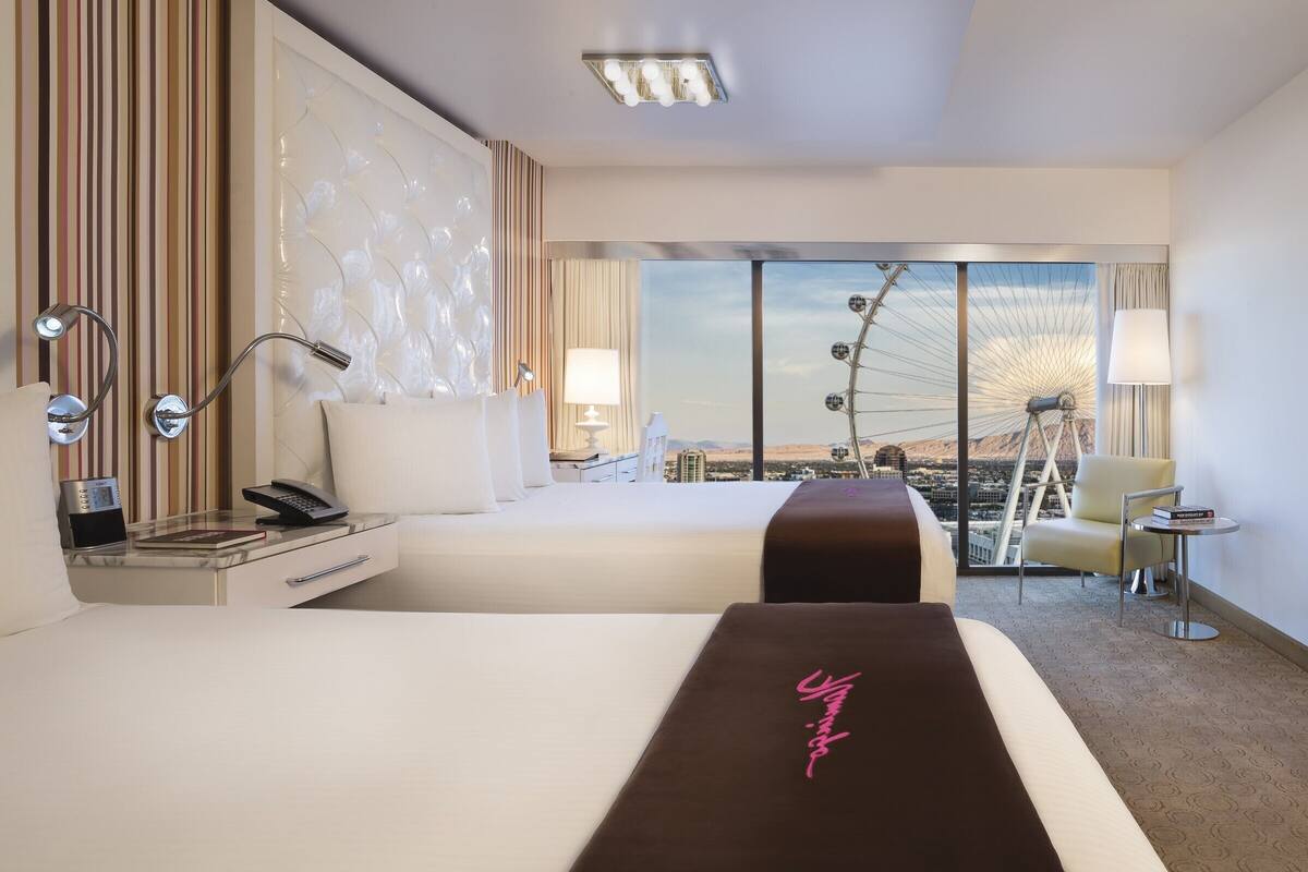 A hotel room with two beds, a desk, a chair, a TV, and a view of a Ferris wheel.