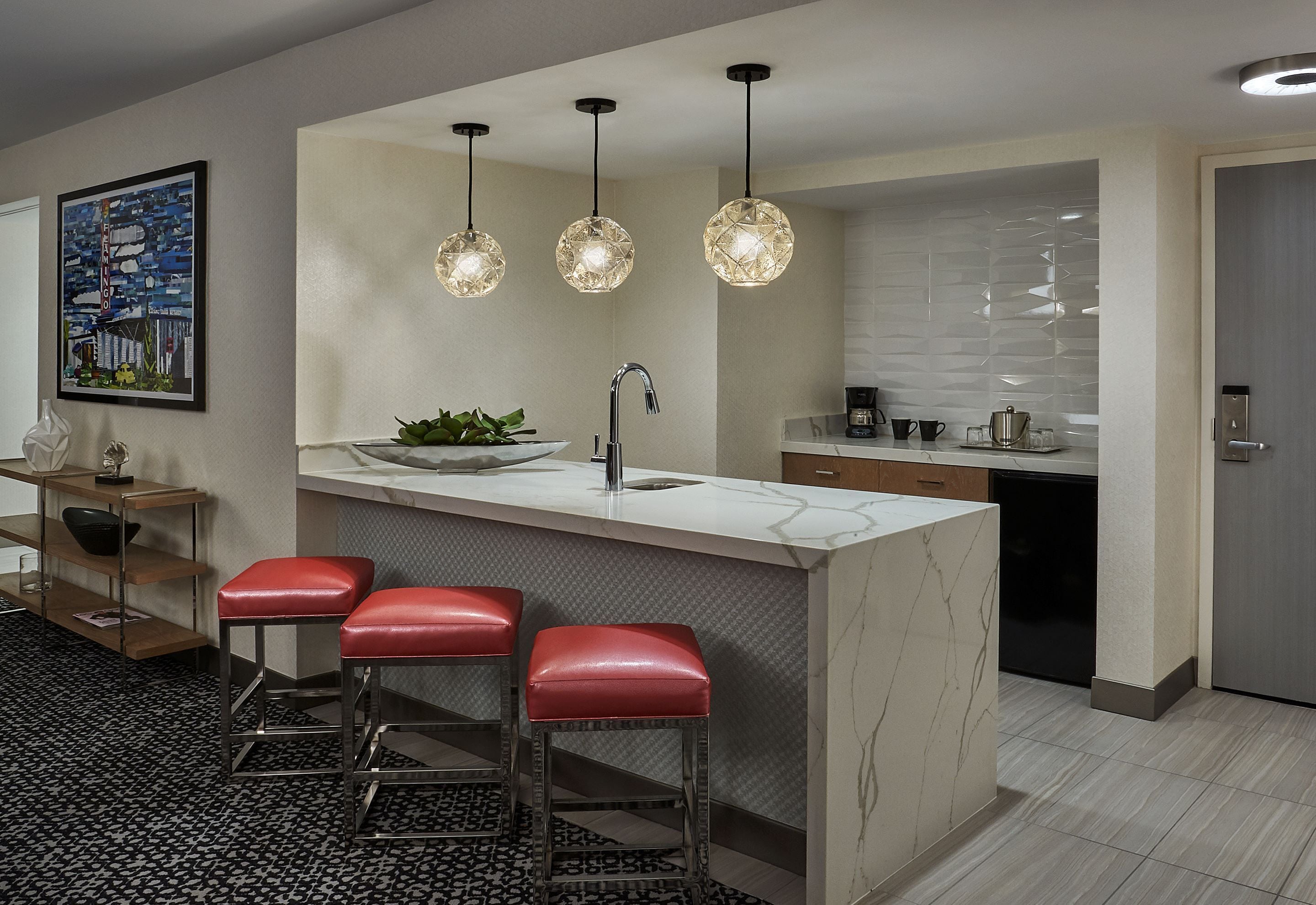 A modern kitchen with a marble countertop, a sink, a coffee maker, and three pendant lights.