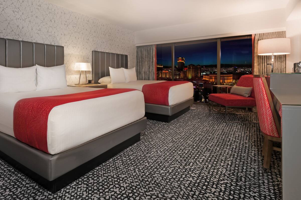 A hotel room with two beds, a city view, a desk, and a chair.