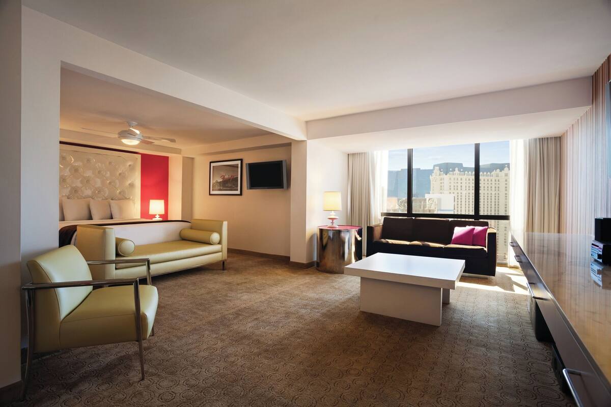 A hotel room with a sofa, armchair, coffee table, TV, and a city view.