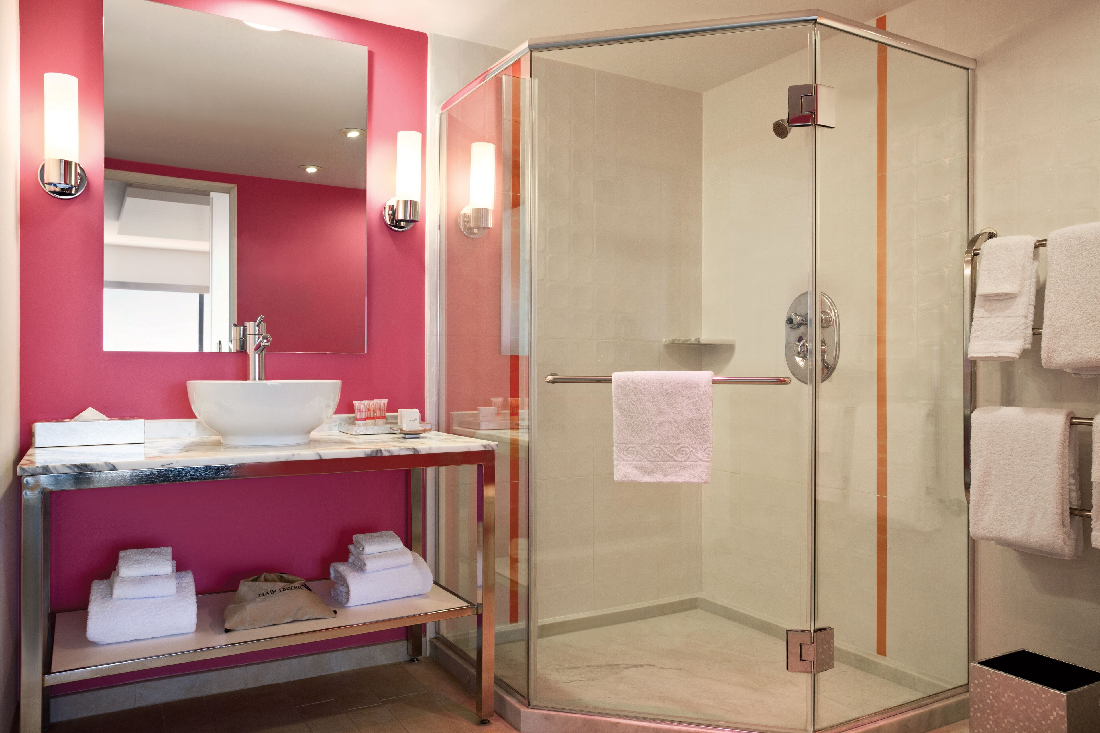 A modern bathroom with a glass-enclosed shower, a marble sink, and a pink wall.