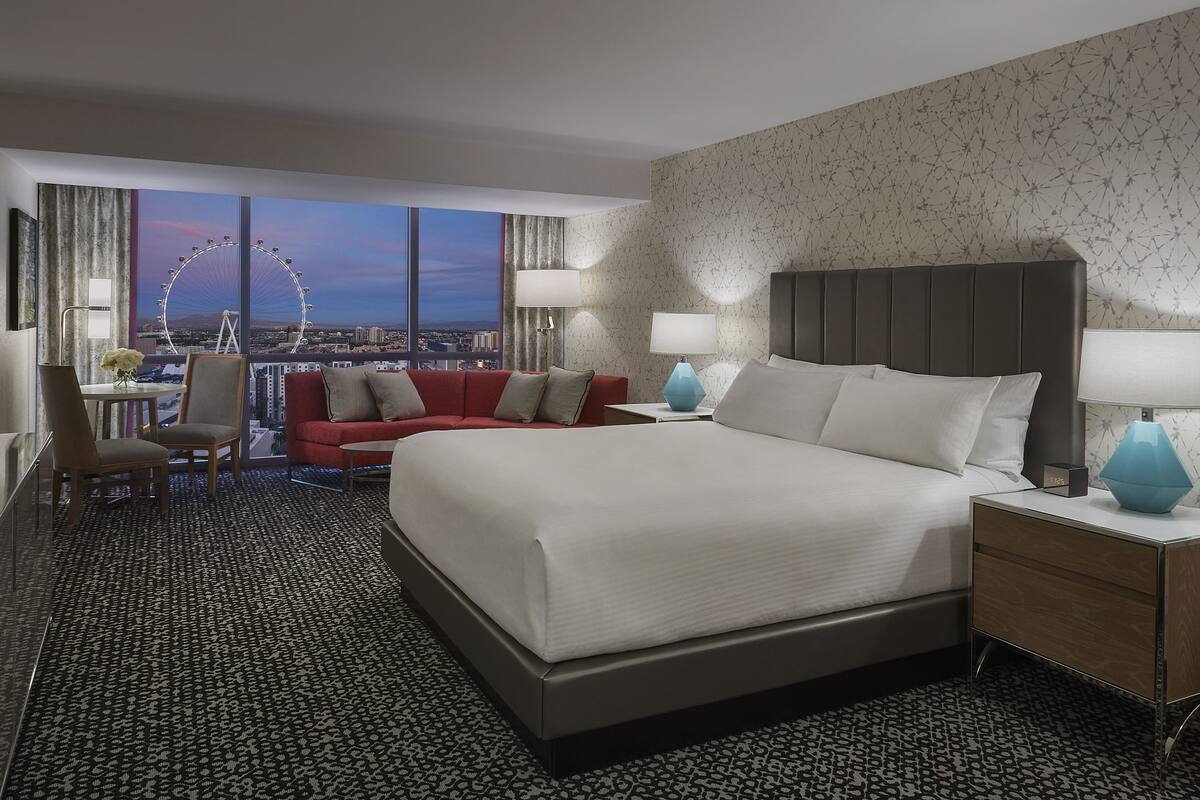 A modern hotel room with a large bed, a red sofa, a desk with a chair, and a view of a Ferris wheel.
