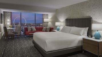 A modern hotel room with a large bed, a red sofa, a desk with a chair, and a view of a Ferris wheel.
