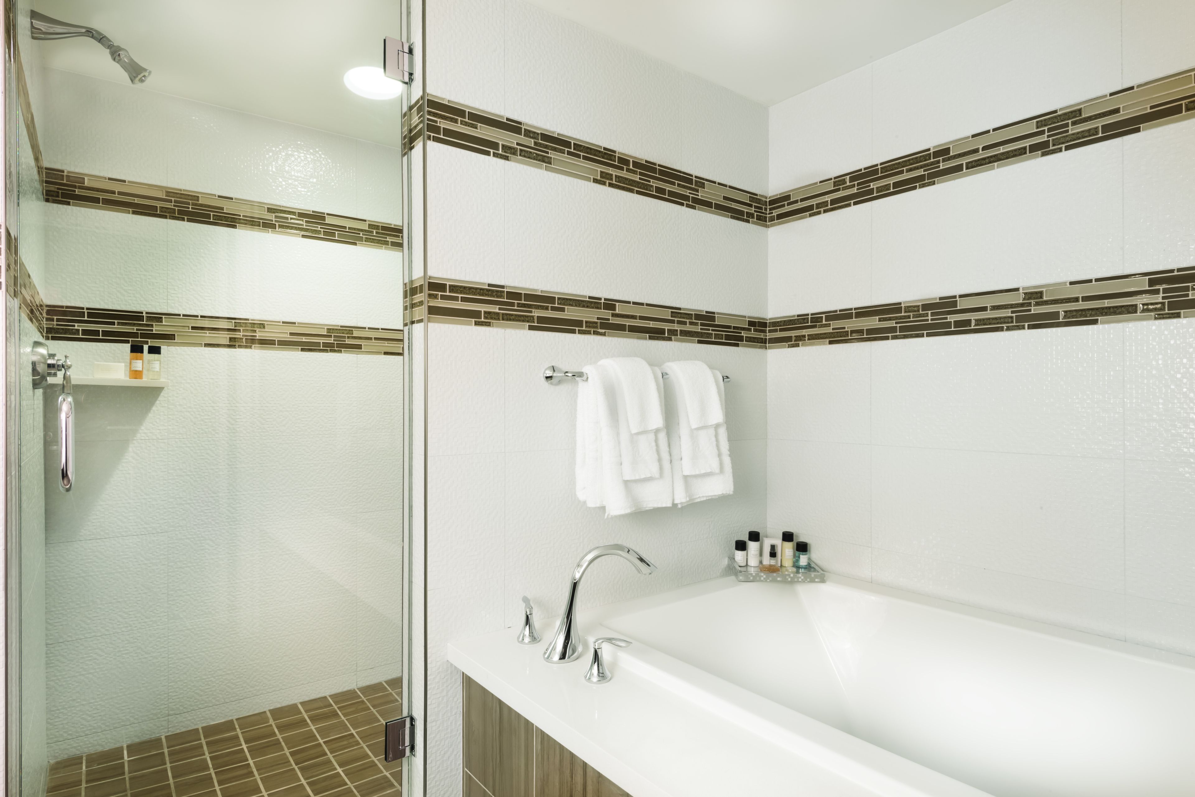 Un baño moderno con cabina de ducha de vidrio, una bañera blanca y un salpicadero de azulejos.