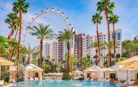 A hotel pool with a Ferris wheel, palm trees, and modern buildings in the background.