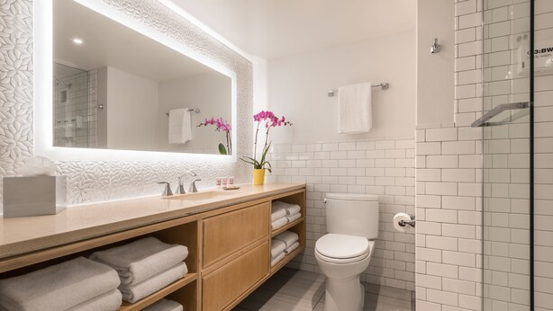 A modern bathroom with a large mirror, white tiles, a wooden vanity, a toilet, and a glass shower enclosure. - Flamingo Las Vegas Hotel & Casino (Las Vegas)