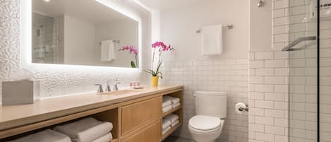 Een moderne badkamer met een grote spiegel, witte tegels, een houten wastafelmeubel, een toilet en een douchecabine met glazen wanden.