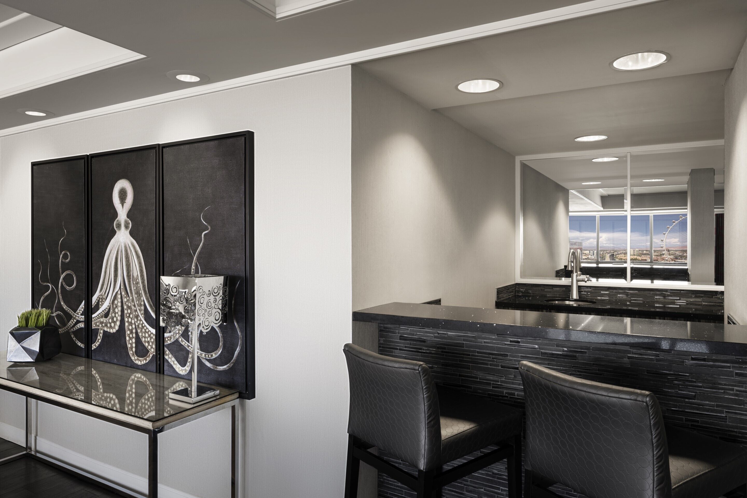 A modern kitchen with a black countertop, a large window, and a bar area with two chairs.