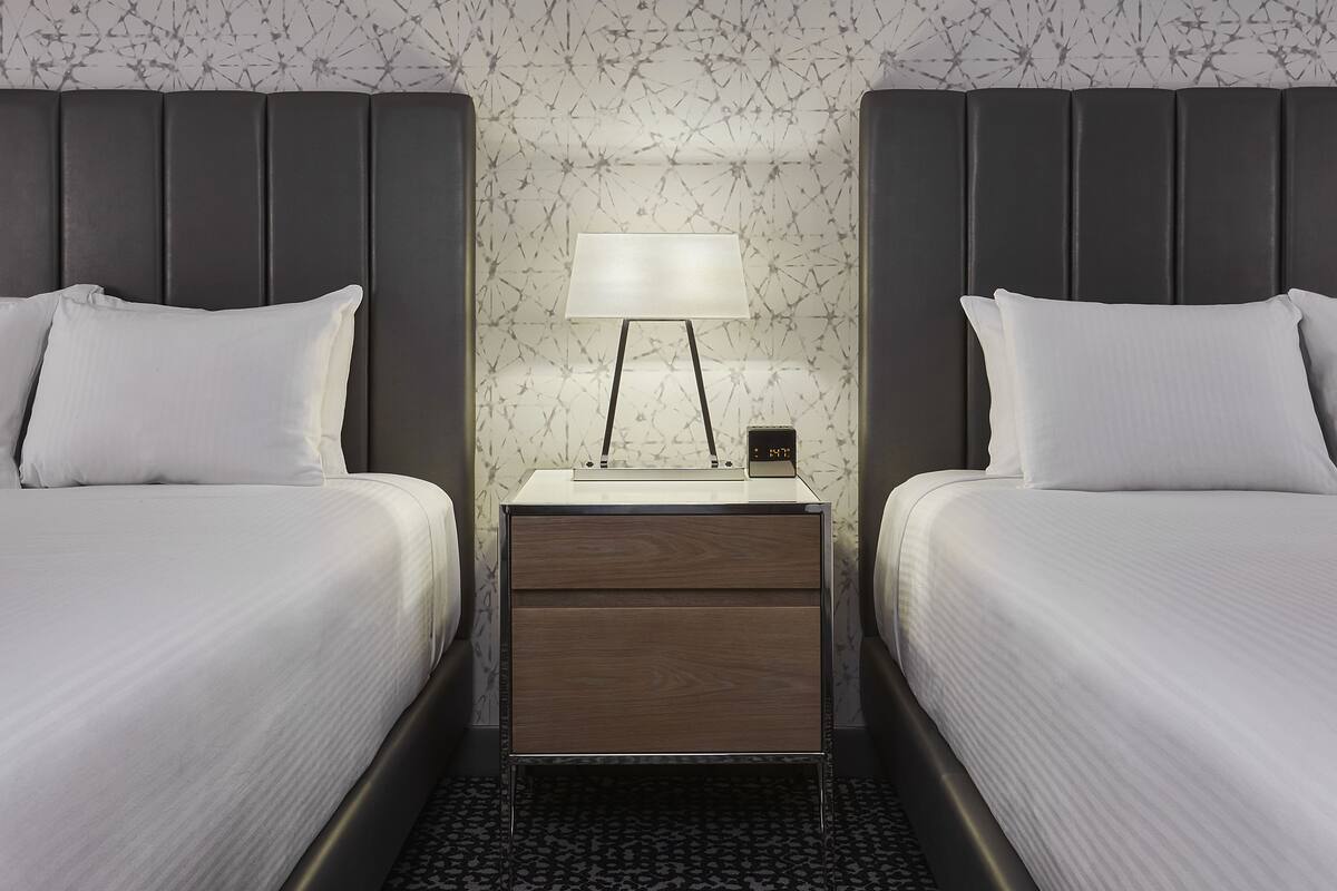A hotel room with two beds, a nightstand with a lamp, and a digital clock.