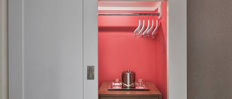 A closet with a red interior, a metal pot on a tray, and a clothing rack with hangers.