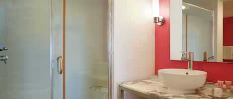 Un baño moderno con cabina de ducha de vidrio, un lavabo blanco con encimera de mármol y una pared de acento roja.