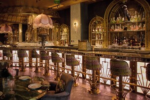 A bar area with ornate chandeliers, a variety of bottles, and a seating arrangement with patterned chairs.