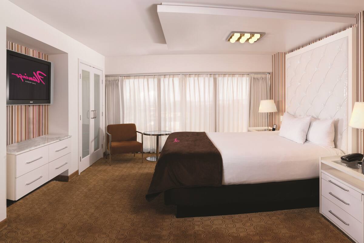 A hotel room with a bed, a TV, a desk, a chair, and a window with curtains.
