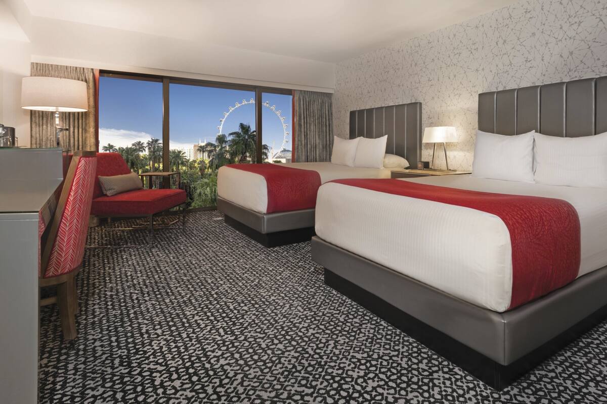 A hotel room with two beds, a desk, a chair, and a view of a Ferris wheel.