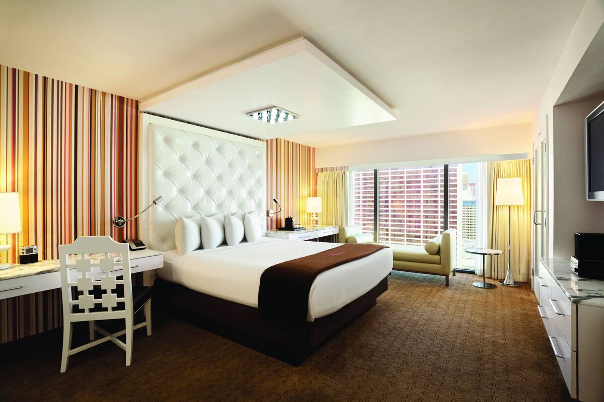 A hotel room with a large bed, a desk, a chair, a TV, and a window with curtains.