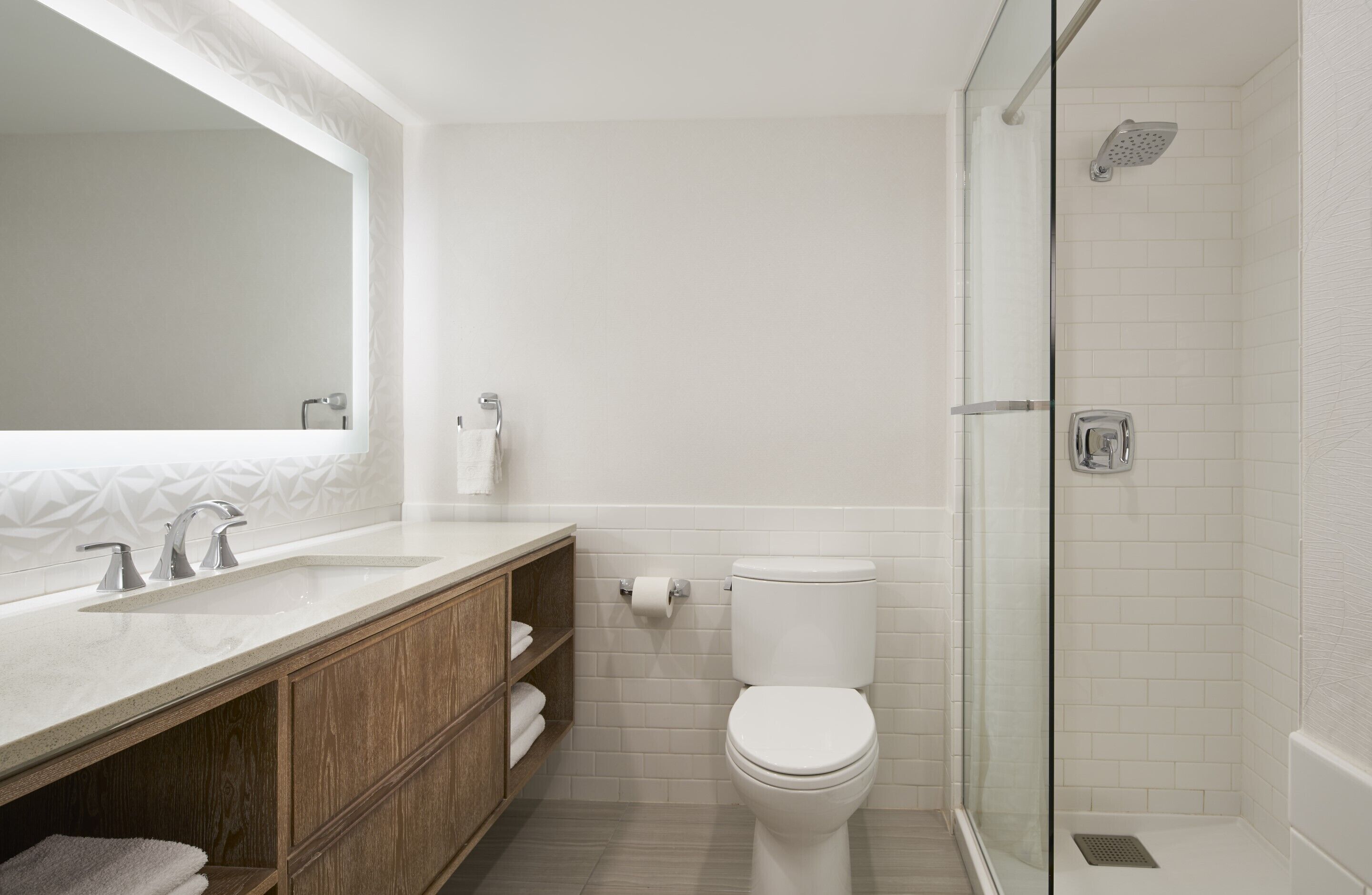 Un baño moderno con un espejo grande, dos lavamanos, un inodoro y una ducha con mampara de vidrio.
