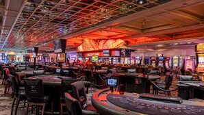 A casino with multiple gaming tables and slot machines, a prominent Bugsy's Bar sign, and a ceiling with a grid pattern.