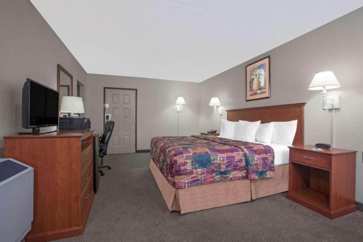 A hotel room with a bed, desk, television, and lamps.