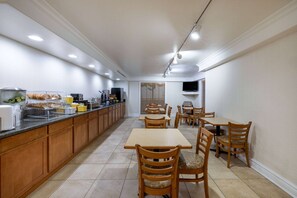 A hotel kitchen with wooden cabinets, a buffet counter, and a dining area with tables and chairs.