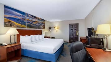 Habitación de hotel con una cama grande, un escritorio, una silla, una lámpara de escritorio, un teléfono, un televisor y un cuadro en la pared.