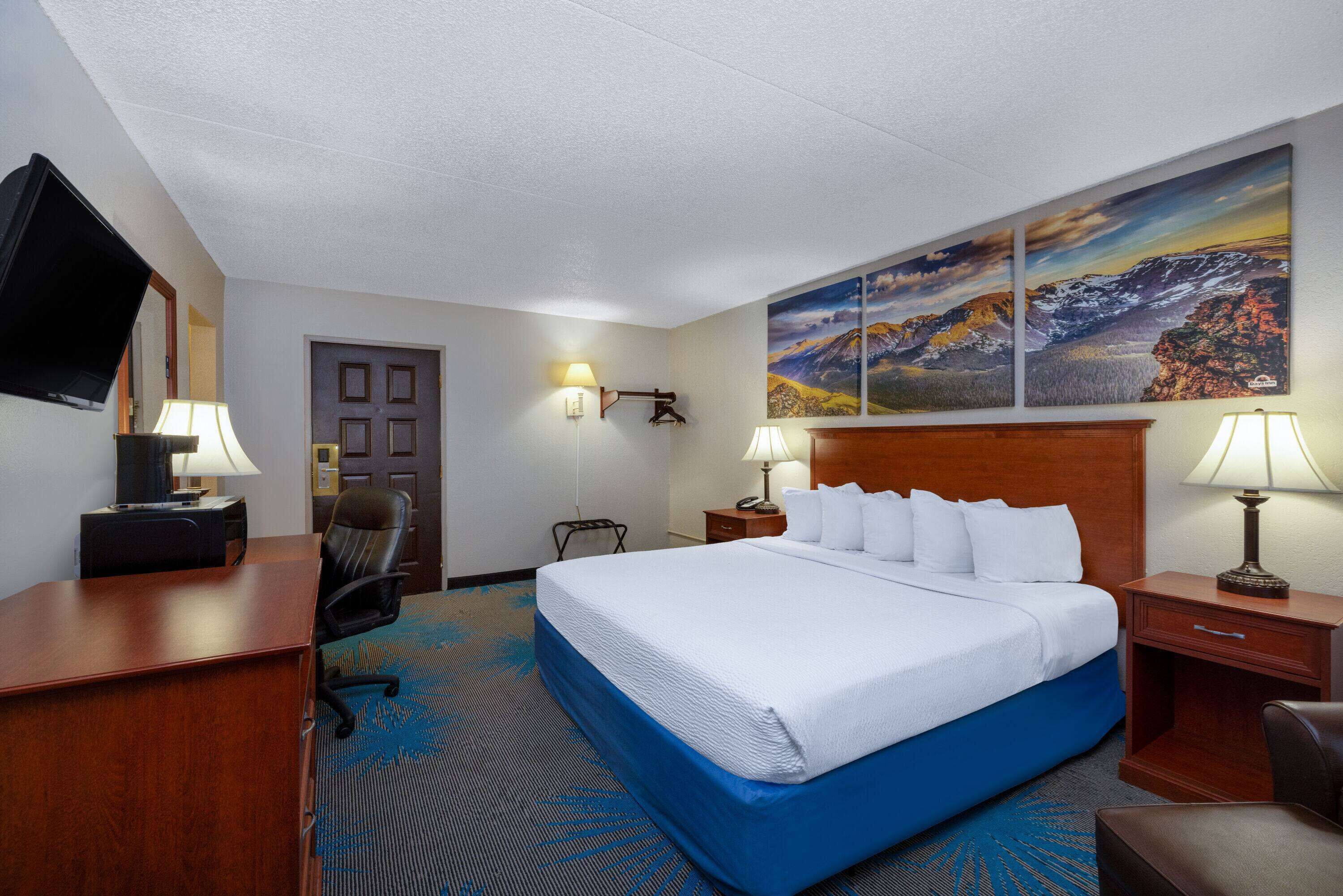 A hotel room with a large bed, a desk, a chair, a TV, and a painting on the wall.
