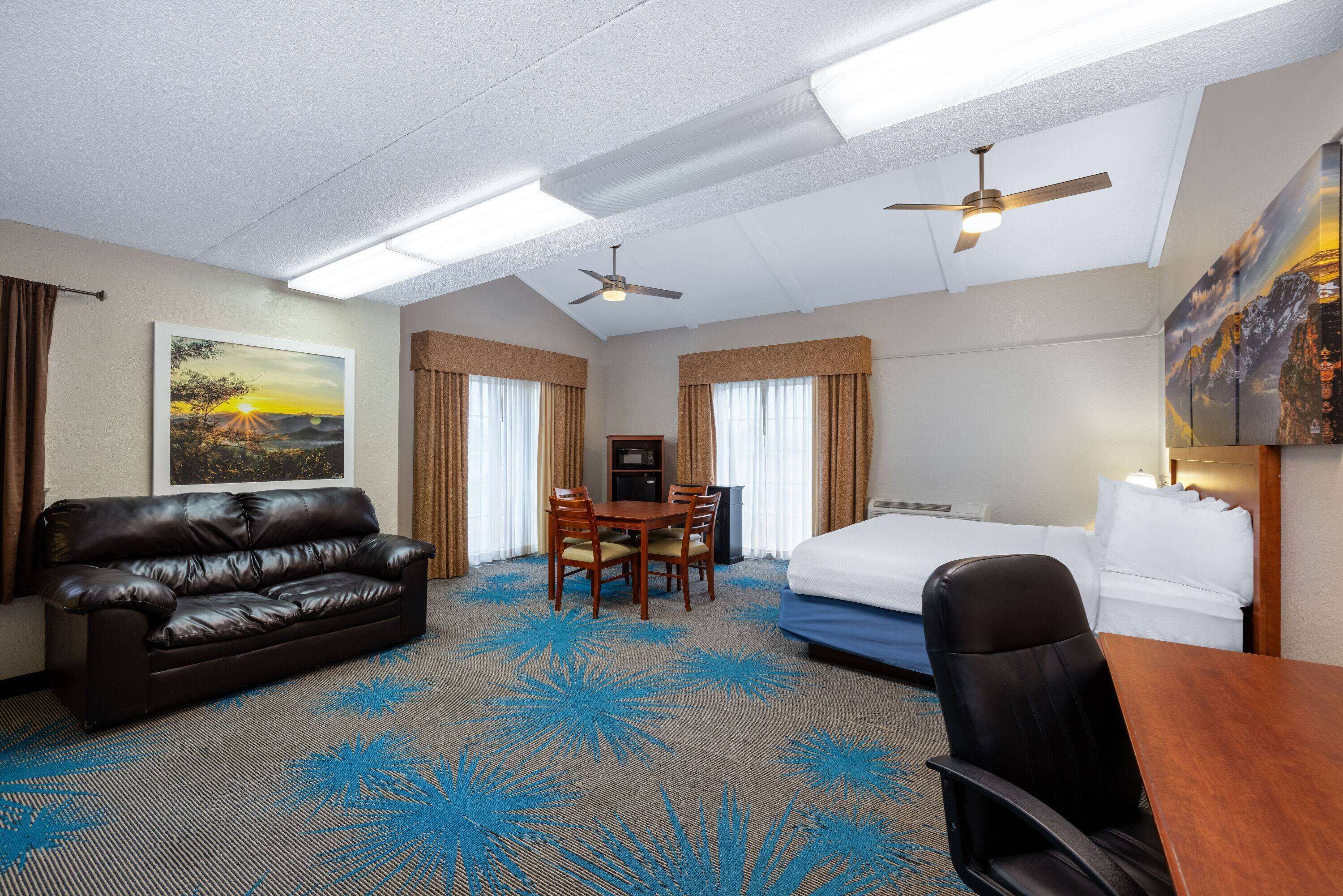 A hotel room with a bed, a desk, a leather sofa, and a dining table.
