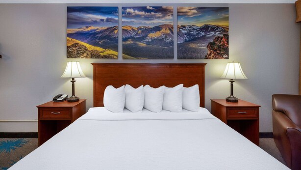 A hotel room with a large bed, two nightstands, a wooden headboard, and three landscape paintings on the wall. - Days Inn by Wyndham Casper (Casper)