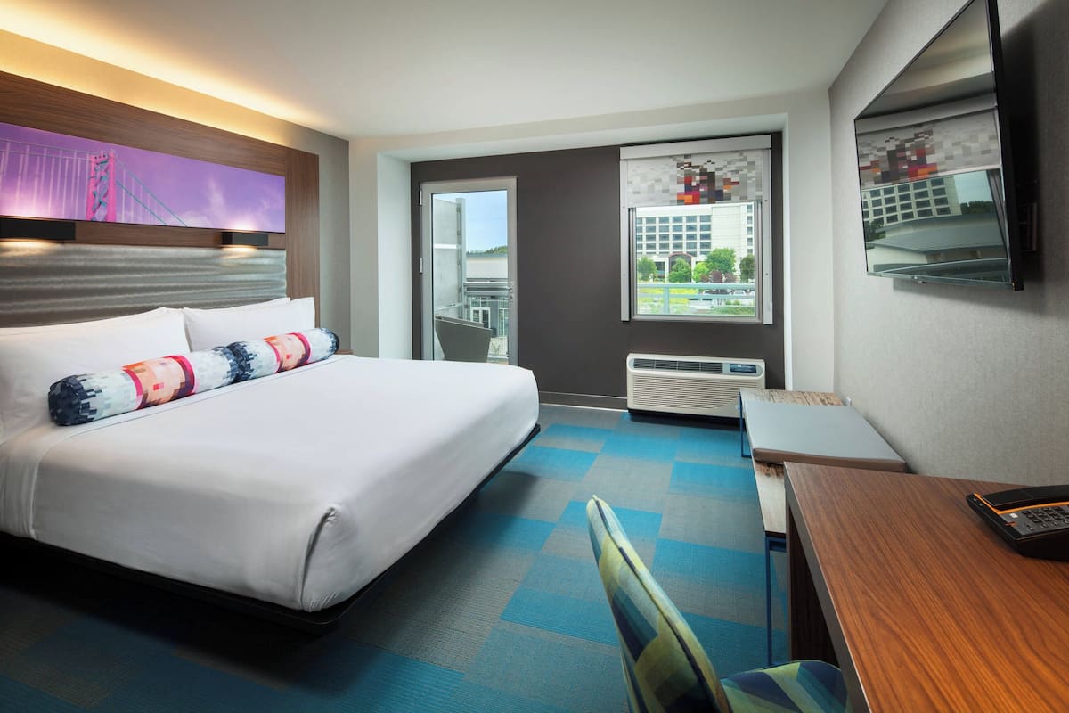 A hotel room with a bed, a desk, a chair, a window with a view, and a mounted TV.