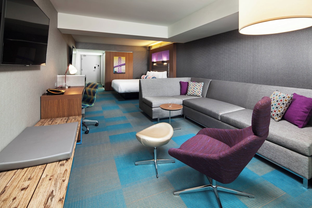 A hotel room with a sofa, armchair, desk, and a bed.