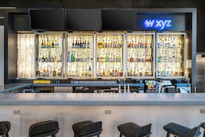 Een bar met een neonbord waarop 'wxyz' staat en planken vol met verschillende flessen.