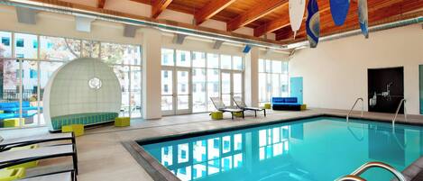 Una piscina interior con techo de madera, ventanas amplias y sillones de descanso.