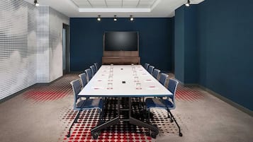 A conference room with a large table, chairs, a screen, and a patterned carpet.