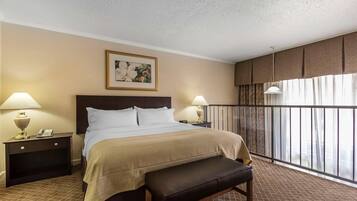 Habitación de hotel con una cama grande, dos mesitas de noche con lámparas, un banco, un cuadro en la pared y un balcón con vistas.
