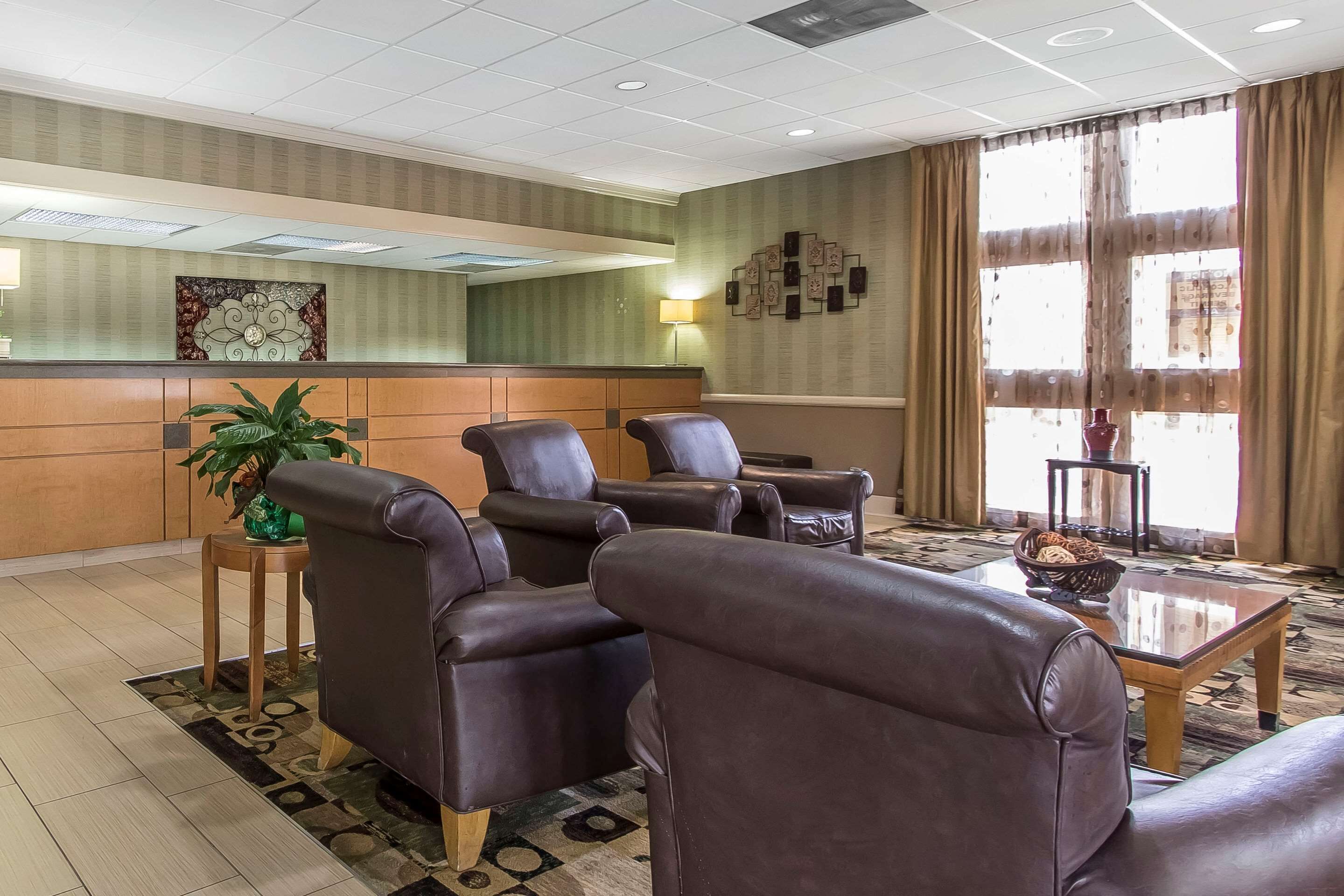 Un vestíbulo de hotel con sillones de cuero, un mostrador de recepción, un amplio ventanal con cortinas y una alfombra estampada.