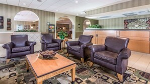A lobby with leather armchairs, a wooden coffee table, patterned carpet, and a reception desk. - Clarion Inn Morgan City (Morgan City)