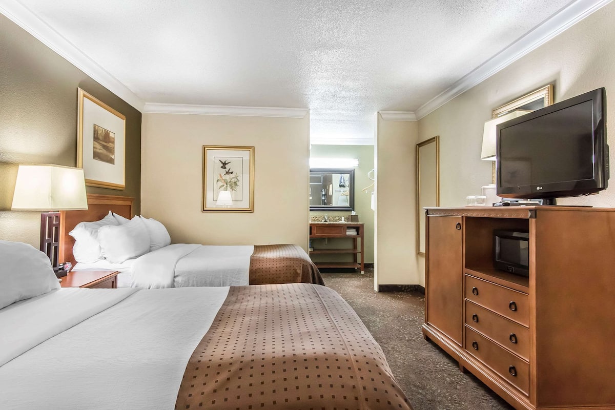 A hotel room with two beds, a TV on a wooden cabinet, and a desk with a lamp.