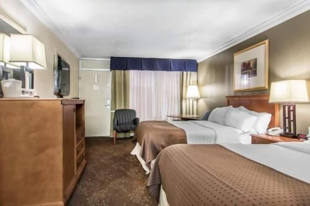 A hotel room with two beds, a desk, a chair, a wardrobe, and a door.