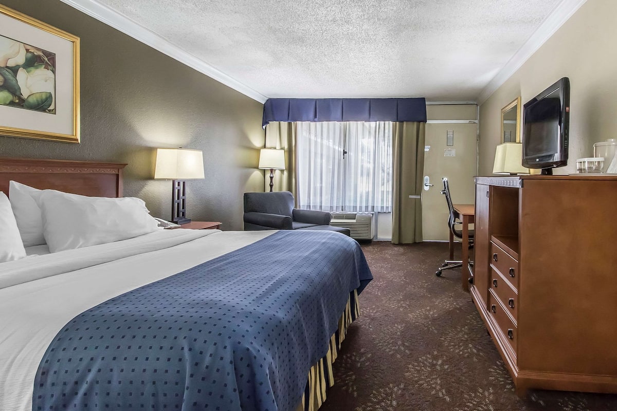 A hotel room with a large bed, a desk with a computer, a chair, a television, and a dresser.
